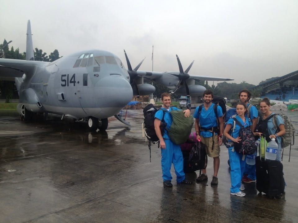 The team in scrubs with backpacks beside a C-130 on a rain-soaked runway