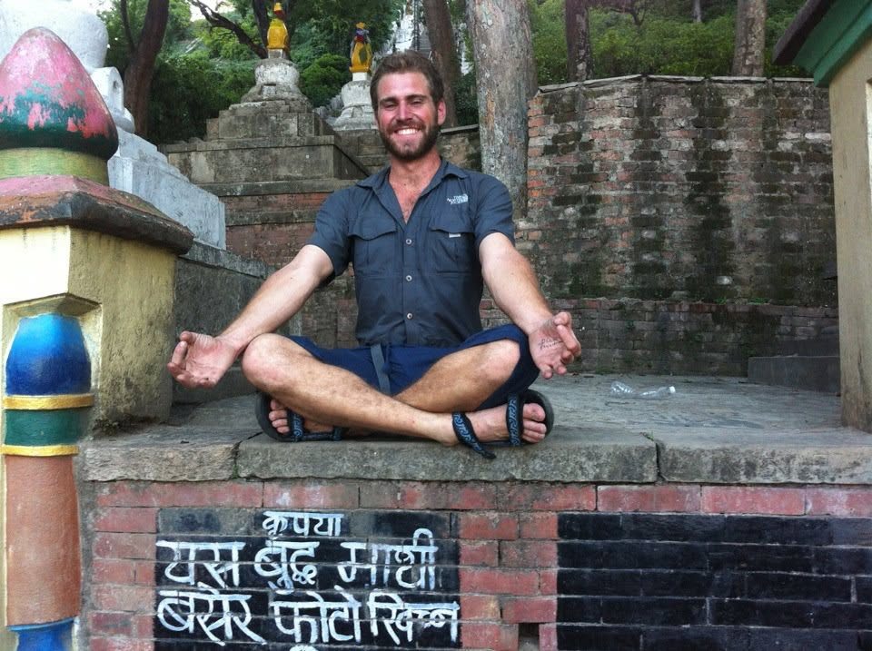 Sitting cross-legged on a brick wall beside a stupa in Nepal